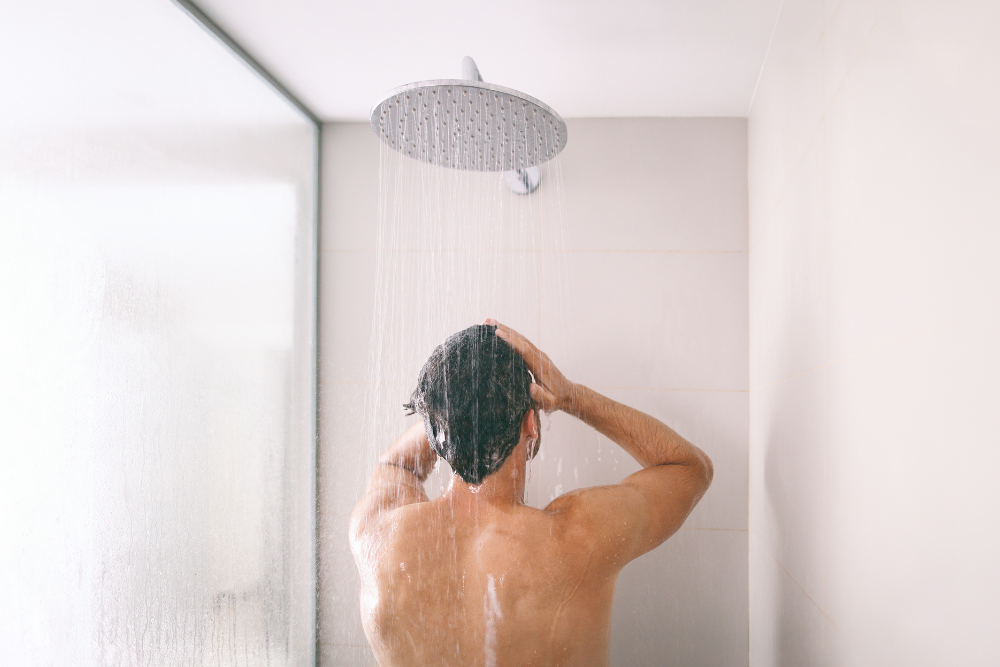 Should You Ice Your Face After a Hot Shower1 | Icelift Rear view of a shirtless man washing his hair under a large rain showerhead in a minimalist shower Stall