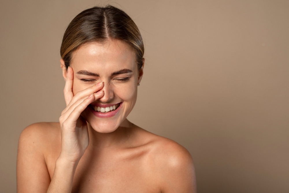 Should You Ice Your Face After a Hot Shower3 | Icelift Smiling woman with eyes closed pinching her nose with her right hand against a beige background